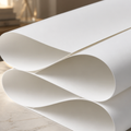 A close-up of a rolled sheet of white material, likely vinyl or paper, draped over a light marble surface with a softly blurred indoor background.