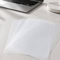 A stacked vellum, fanned out on a light gray desk, with a blurred laptop and lamp in the background.